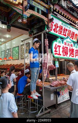 Chinesischer Mann Schnitzerei Fleisch aus Lamm Karkasse Skelett hängen für Verkauf im Street Food Vendor Shop im muslimischen Viertel Xian XI'an ChinaMuslim Viertel Xian Stockfoto