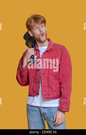 Junger bärtiger Mann in roter Jacke mit Ukulele Stockfoto