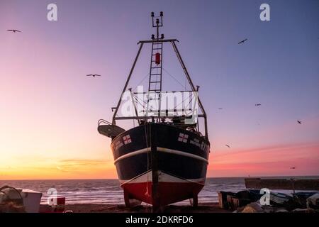 Hastings; East Sussex; Großbritannien. Dezember 2020. Farbenprächtiger Sonnenaufgang, während Möwen an einem luftigen, aber milden und sonnigen Tag über dem Fischerboot schweben. Carolyn Clarke/Alamy Live News Stockfoto