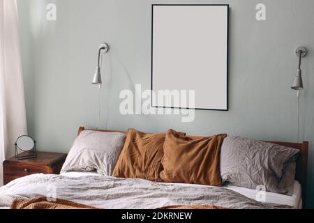 Portrait schwarz Bilderrahmen Mockup und silberne Lampen auf sage grüne Wand. Blick auf das Schlafzimmer. Graue Bettwäsche und rostige Musselin-Kissen auf Holzbett. Spiegelung ein Stockfoto