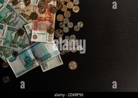 Viele russische Metallmünzen und Papiergeld lügen Auf einem schwarzen Holztisch Stockfoto