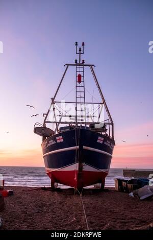 Hastings; East Sussex; Großbritannien. Dezember 2020. Farbenprächtiger Sonnenaufgang, während Möwen an einem luftigen, aber milden sonnigen Tag über dem Fischerboot schweben. Carolyn Clarke/Alamy Live News Stockfoto