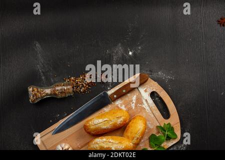fresh wheat white bread on a cutting board with seasonings sprinkled with flour on a black wooden table Stock Photo