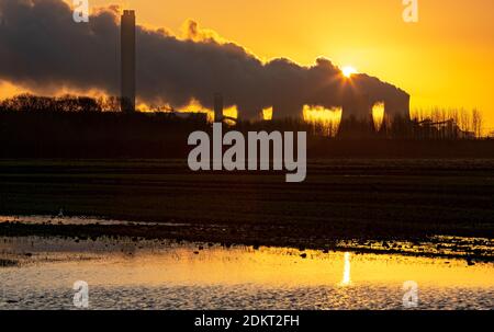 Sonnenaufgang bei Drax. Ein Wintermorgen mit der Sonne, die kurz vor dem Aufgehen hinter einer Wasserdampfspur steht, die aus den Kühltürmen eines Kraftwerks aussendet Stockfoto