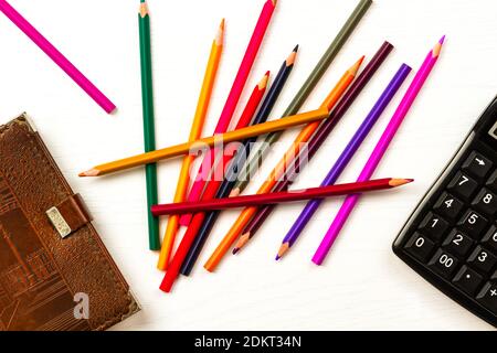 colored pencils and brown leather diary lie on a white wooden table Stock Photo