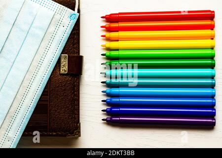 brown diary and medical mask and bright colored markers without caps lie on a white wooden table Stock Photo