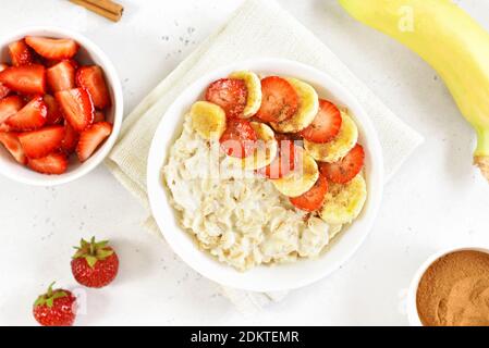 Haferflocken Haferbrei mit Erdbeere, Banane in Schüssel über weißem Stein Hintergrund. Draufsicht, flach liegend Stockfoto