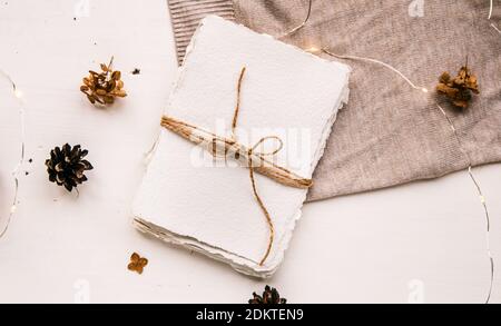 Flach liegend im Hygge-Stil. Weihnachtswunsch. Handgemachtes Papier mit Bastelfaden gebunden. Briefumschlag, Tannenzapfen, Bastelfaden. Selektiver Fokus Stockfoto