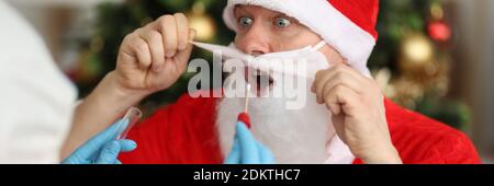 Arzt in Schutzanzug unter Abstrich pcr von santa claus In der Nähe von Weihnachtsbaum Stockfoto