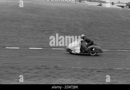 1960s, historisch, Motorsport, Sidecar Racing, ein Motorradfahrer und Sidecar Passagier auf ihrem Fahrzeug - nummeriert vier - auf der Rennstrecke, England, Großbritannien. Sidecar Racing ist ein Sport mit einem maßgeschneiderten 3-Rad-Motorrad und ist die einzige Form des Motorsports, wo der Passagier und Fahrer beide das Fahrzeug steuern. Das Fahrzeug fährt mit hohen Geschwindigkeiten und der Sport ist spannend zu beobachten. Sowohl Fahrer als auch Beifahrer tragen die traditionellen schwarzen Lederoutfits der Zeit. Stockfoto