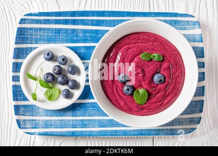 Blueberry and banana smoothie bowl with yogurt, cashew, chia seeds, and flax seeds on a white wooden background with ingredients, top view, close-up Stockfoto