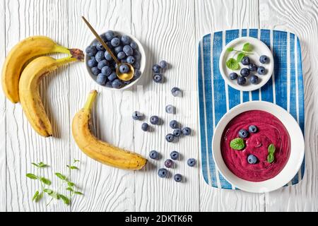 Blueberry and banana smoothie bowl with yogurt, cashew, chia seeds, and flax seeds on a white wooden background with ingredients, top view, close-up Stockfoto