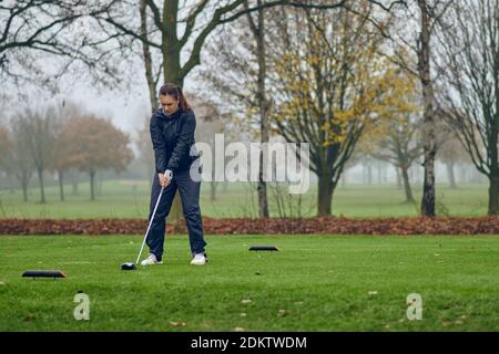 Frau mittleren Alters spielt Golf an einem kalten nebligen Wintertag Auf einem Parklandkurs abzweigt und ihr Schuss anlegt Stockfoto