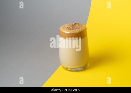 Dalgona Kaffee mit üppigem Schaum in einem Glas auf einem gelben und grauen Hintergrund. Trendiges Koreanisches Getränk Stockfoto