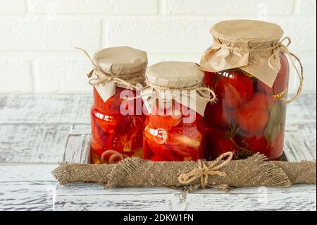 Gläser mit Tomaten aus der Dose mit Knoblauch und Pfeffer. Fermentierte Nahrung auf weißem Holzhintergrund. Stockfoto