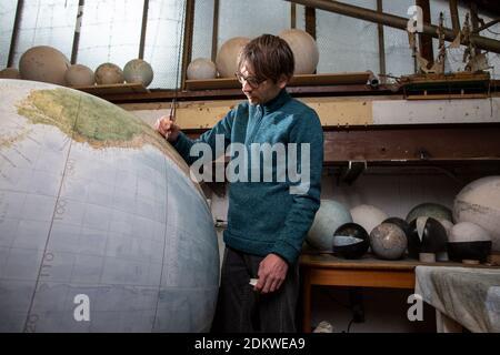 Eine Menschenhand malt einen Chruchill Globe, den größten handgefertigten Globus der Welt mit einem Durchmesser von 50 cm, bei Bellerby & Co in Stoke Newington, North London, UK Stockfoto