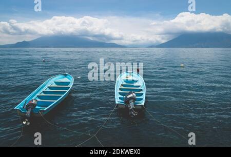 Zwei blaue Boote auf dem dunkelblauen See Atitlan mit Blick auf die Vulkane San Pedro und Toliman in Santa Cruz la Laguna, Guatemala Stockfoto