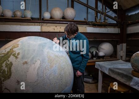 Eine Menschenhand malt einen Chruchill Globe, den größten handgefertigten Globus der Welt mit einem Durchmesser von 50 cm, bei Bellerby & Co in Stoke Newington, North London, UK Stockfoto