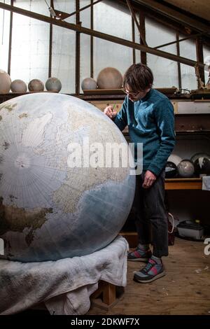 Eine Menschenhand malt einen Chruchill Globe, den größten handgefertigten Globus der Welt mit einem Durchmesser von 50 cm, bei Bellerby & Co in Stoke Newington, North London, UK Stockfoto
