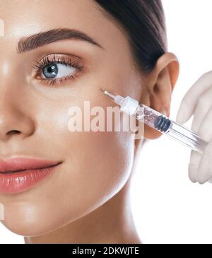 Beautiful woman during facial mesotherapy for smoothing of mimic wrinkles around eyes. Beautician doing anti-aging injection for rejuvenation and lift Stock Photo