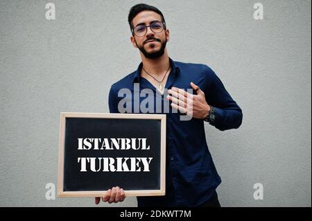 Araber tragen blaues Hemd und Brillen halten Brett mit Istanbul Türkei Inschrift. Größte Städte in der islamischen Welt Konzept. Stockfoto