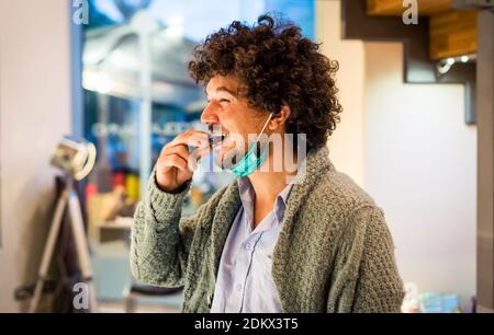 Nahaufnahme eines Latino-lockigen Mannes, der süß isst Schokolade tragen warme Winterkleidung während der weihnachtsferien in einem Shop.Happy Person beißt Stockfoto