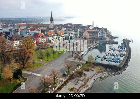 Friedrichshafen, Deutschland. Dezember 2020. Nur wenige Leute laufen mittags auf der Seepromenade (mit Drohne aufgenommen). Im Hintergrund ist die Innenstadt von Friedrichshafen und der Bodensee zu sehen, der noch im Nebel liegt. Im Kampf gegen die Corona-Pandemie hat am 16. Dezember 2020 um 0:00 Uhr in Deutschland eine harte Sperre begonnen. Einzelhändler müssen landesweit schließen, mit Ausnahme nur für Geschäfte, die den täglichen Bedarf erfüllen. Quelle: Felix Kästle/dpa/Alamy Live News Stockfoto