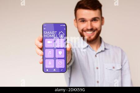 Happy Millennial Mann zeigt Handy mit smarthome Automation Control System auf dem Bildschirm, weißer Hintergrund Stockfoto