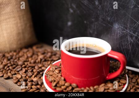 Rote Tasse Kaffee mit Kaffeebohnen auf dunklem strukturiertem Hintergrund. Morgens frisches Energiekonzept. Stockfoto