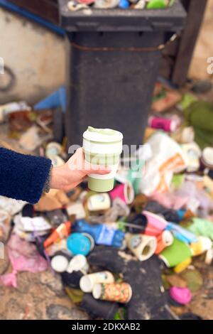 Weibliche Hand hält wiederverwendbare Öko-Cup und eine Menge Müll auf dem Hintergrund Stockfoto