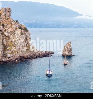 Segelyacht und Boot segeln entlang der felsigen Küste des Schwarzen Meeres zwischen Klippen und Bergen. Naturlandschaft und Seenlandschaft. Menschen reisen und haben va Stockfoto