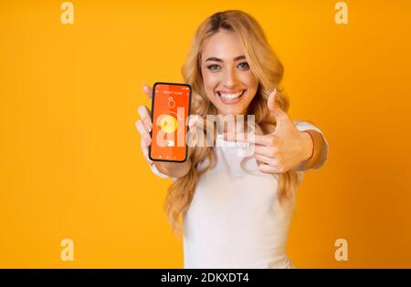 Junge Dame zeigt auf Handy mit smarthome App auf dem Bildschirm, Temperatur über orangenen Hintergrund, Collage Stockfoto