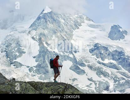 Horizontale Momentaufnahme des Wanderers mit Wanderstöcken im Vordergrund. Sagenhaft felsiger Ober Gabelhorn im Schnee in den Pennine Alpen in der Schweiz, zwischen Zermatt und Zinal gelegen Stockfoto