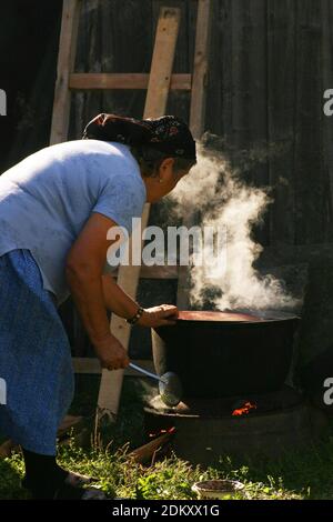 Vrancea County, Rumänien. Frau, die im Freien in einem großen Kessel über dem Feuer kocht. Stockfoto