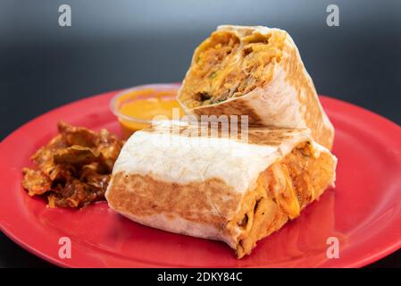 Huhn Burrito mit frischem Fleisch in zwei Hälften geschnitten geladen und präsentiert auf einem roten Teller. Stockfoto