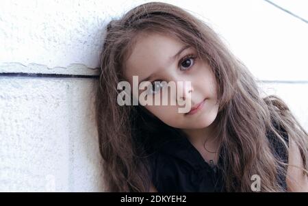 Portrait of a Little cute girl with big eyes leaning on wall Stock Photo