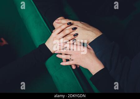 Zwei Mann und drei Frauen halten die Hände auf einem Tisch, was eine polyamorische Beziehung oder ein Liebesdreieck impliziert Stockfoto