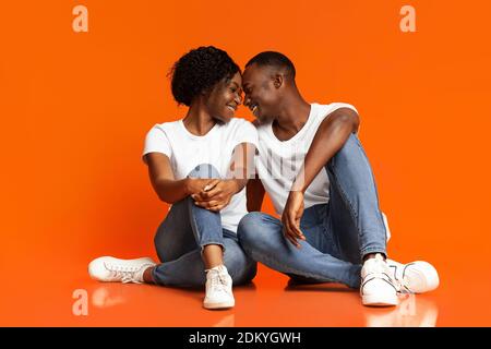 Emotionale schwarze Liebhaber kuscheln auf orangefarbenem Hintergrund Stockfoto