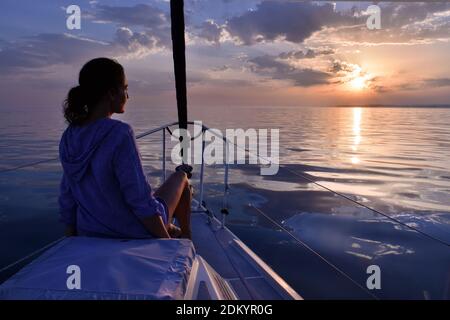 Frau, die sich auf dem Segelboot während des ruhigen Sonnenuntergangs auf dem Meer entspannt Stockfoto