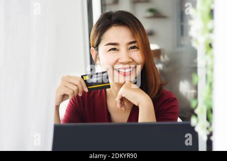 Schöne asiatische Frau Hand hält Kreditkarte und mit Laptop Für Online-Shopping lächelnd zur Kamera Stockfoto