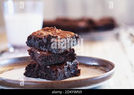 Frisch zubereitete hausgemachte fudgy Brownies auf einer Untertasse über einem weißen rustikalen Holztisch gestapelt. Extrem geringe Schärfentiefe mit unscharfem Hintergrund und einem Stockfoto