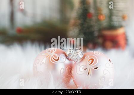 Zwei rosa Weihnachtsschmuck auf einem weißen Teppich. Selektiver Fokus mit weihnachtlichen Bäumen im Hintergrund. Stockfoto