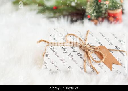 Eingewickeltes Weihnachtsgeschenk. Das Geschenk wurde mit einem braunen Garn mit einem Papieranhänger gebunden. Selektiver Fokus mit verschwommenem Hintergrund und fallendem Schnee. Stockfoto