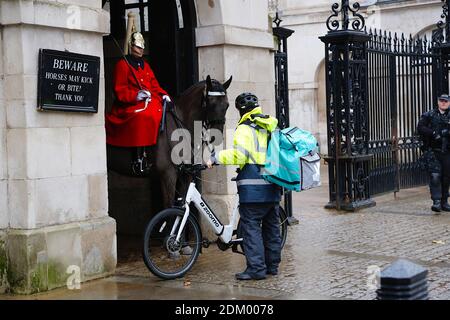 Westminster, London, Großbritannien. 16 Dez 2020. UK Wetter: Kälter und nieseliger Regen im Westminster in London. Ein deliveroo-Zusteller mit einem Zoomo-Elektrofahrrad bittet einen Pferdewächter um Anweisungen, während ein Polizeibeamter am Tatort erscheint. Bildnachweis: PAL Media /Alamy Live News Stockfoto