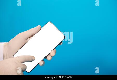Telefon mit leerem Bildschirm-Mockup (für Text oder Bild), in den Händen eines Arztes mit Hygienehandschuhen, Zeigefinger zeigt auf den mobilen Bildschirm Stockfoto