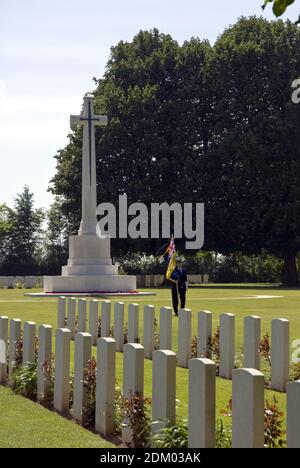 Ein britischer Veteran marschiert mit einer Flagge vom Opferkreuz auf dem Friedhof der Bayeux Commonwealth war Graves Commission, Bayeux, Frankreich. Stockfoto