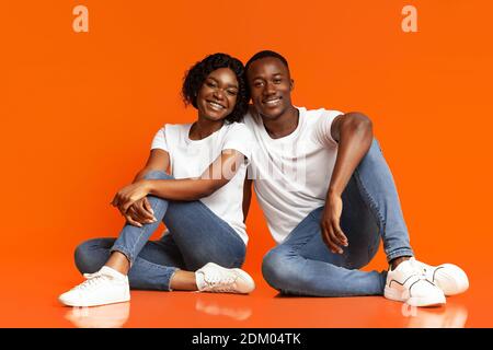 Sorgenfreie afroamerikanische Liebhaber sitzen auf dem Boden, Studioaufnahme Stockfoto