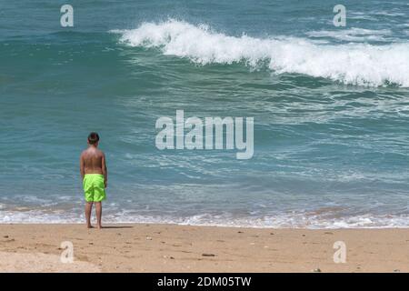 Ein kleiner Junge, der in farbenfrohen Shorts auf einem Kurzurlaub am Fistral Beach in Newquay in Cornwall steht. Stockfoto