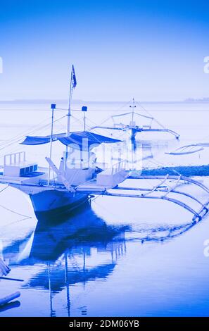 Traditionelle philippinische Ausleger-Fischerboote, die als "bangka"-Boote oder Pumpboote bekannt sind, haben keinen Kiel und sind so konstruiert, dass sie über flache Meere und Korallenriffe driften. Sie sind mit zwei Stützen ausgestattet, um auf rauer See Unterstützung zu bieten. Bangka Boote haben jetzt Rollen reichen von der Beförderung von Waren zu abgelegenen Inseln zu dienen als Touristentaxis zu Tauchen Expeditionsboote und Fähren. Im Bild: bangka Boote liegen in Buyong auf Mactan Island, in Cebu auf den Philippinen. Stockfoto