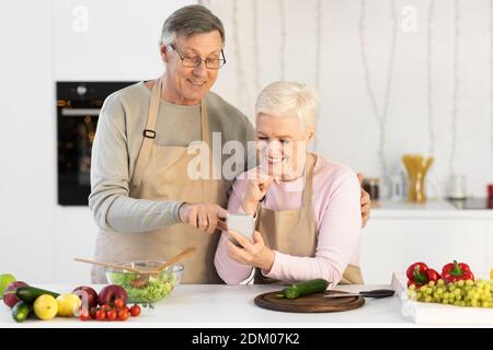 Fröhliche Ältere Ehegatten Mit Handy Kochen Abendessen In Der Küche Stockfoto